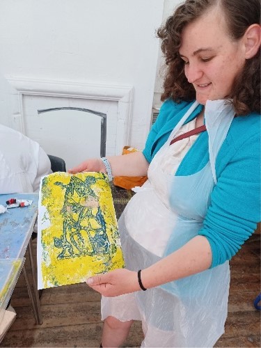 A woman shows a piece of artwork on a canvas using paint to the camera.