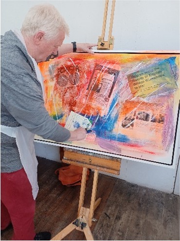 A man is producing artwork on a canvas on an easel using mixed mediums.