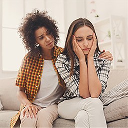 Two young women, one looking concerned, other with face in hands and eyes closed.jpg