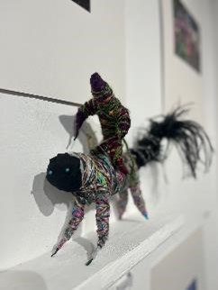 A figurine made of wire, thread and fabrics shaped like an animal and a man riding on top. 