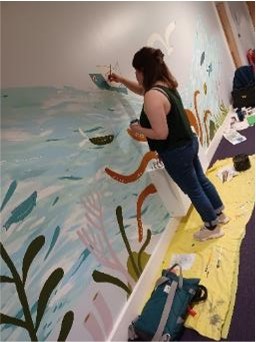 A woman painting a mural on the wall at Severnfields Health Village.