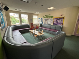Inside the waiting room here is a large sofa which wraps around the edge of the room. In the middle is a table with children's chairs and toys on top.