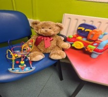 Teddy sat on a blue chair with children's toys