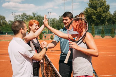 Four people at a tennis court, shaking hands across the net.