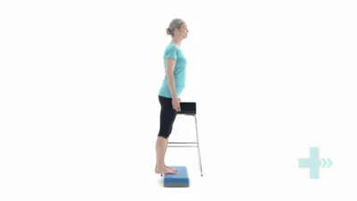 A moving image of a person stood with their feet half on a step, and half off, lowering the heel.