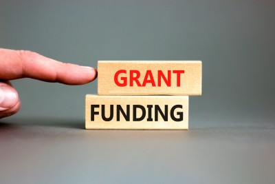 Two wooden blocks which have the words 'Grant' and 'Funding' on each. A finger is pointing at the blocks.