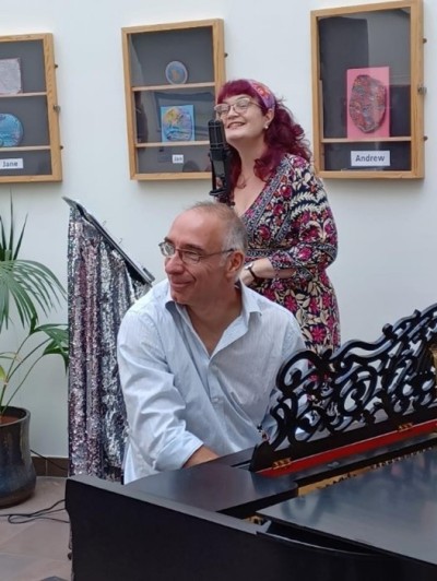 A man playing a piano and a woman behind him singing into a microphone.