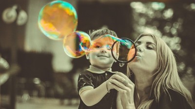A woman standing with a young boy blowing bubbles